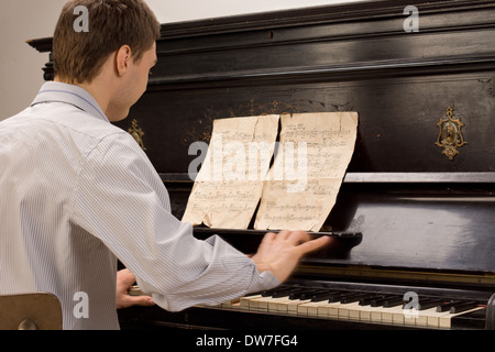 Jeune homme assis auprès de la pianiste jouant du piano une mélodie d'une vieille partition de musique en lambeaux sur un piano droit Banque D'Images