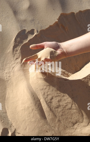 Le sable glisser entre les doigts d'une main de femme dans le désert du Sahara en Tunisie. Banque D'Images