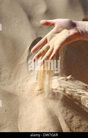 Le sable glisser entre les doigts d'une main de femme dans le désert du Sahara en Tunisie. Banque D'Images