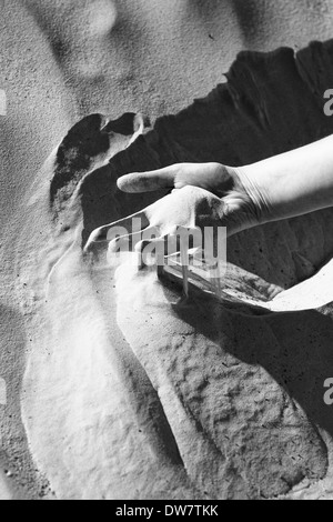 Le sable glisser entre les doigts d'une main de femme dans le désert du Sahara en Tunisie. Banque D'Images