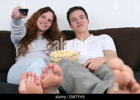 Jeune couple assis sur un canapé, regarder la télévision et eating popcorn Banque D'Images
