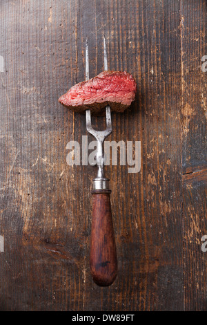 Pièce de boeuf steak sur fourchette à viande sur fond de bois Banque D'Images