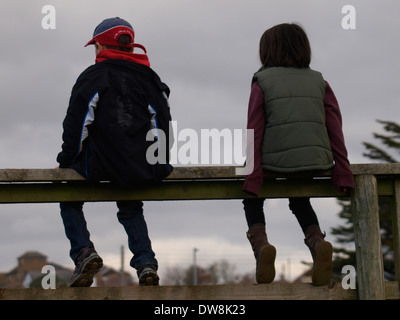 Deux enfants assis sur une clôture regarder match de rugby, Bude, Cornwall, UK Banque D'Images