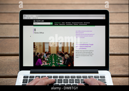 Le site web du Home Office sur un MacBook contre un banc en bois fond de plein air y compris les doigts d'un homme (usage éditorial uniquement). Banque D'Images