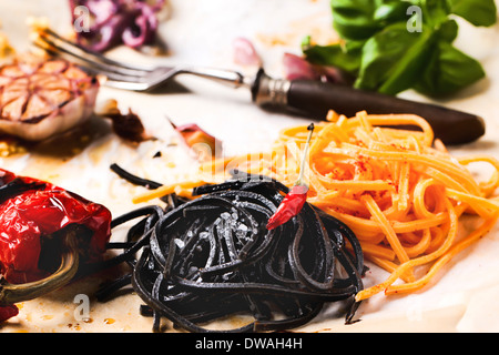 Spaghetti noir et orange servi sur un papier chiffonné avec paprika grillés, ail et basilic frais. Banque D'Images