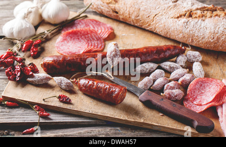 Ensemble de salami saucisses servis avec du pain frais, l'ail et Red Hot Chili Peppers sur planche à découper en bois. Banque D'Images