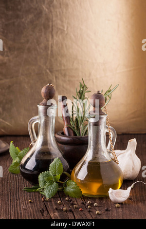 L'huile d'olive et vinaigre dans bouteilles vintage sur la vieille table en bois avec de l'ail, menthe et romarin en mortier vintage Banque D'Images