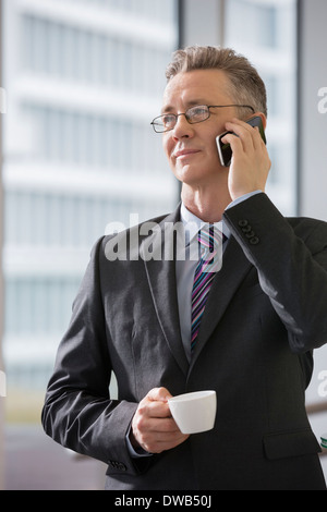 Businessman with coffee cup using cell phone in office Banque D'Images