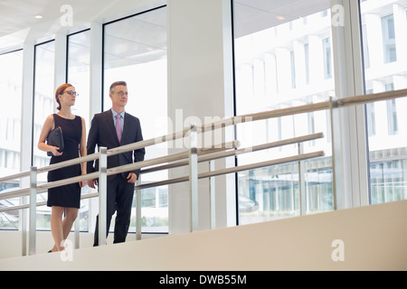Business people walking by railing in office Banque D'Images
