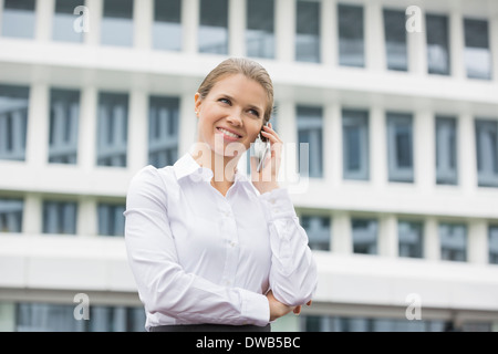Smiling businesswoman using cell phone outside office Banque D'Images