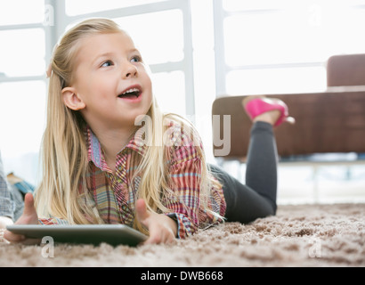 Cute girl with digital tablet à la route en position allongée sur un tapis dans la salle de séjour Banque D'Images