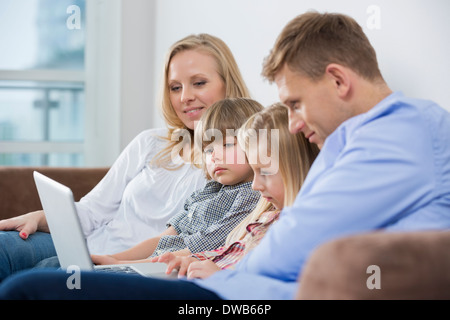 Les parents avec des enfants à l'aide de l'ordinateur portable sur canapé à la maison Banque D'Images