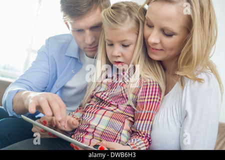 Les parents et la fille using tablet computer in living room Banque D'Images