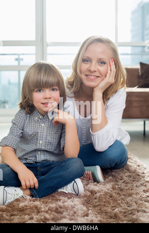 Portrait of happy mother sitting with boy sur un tapis dans la salle de séjour Banque D'Images