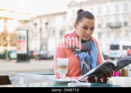 Young woman reading book at sidewalk cafe Banque D'Images