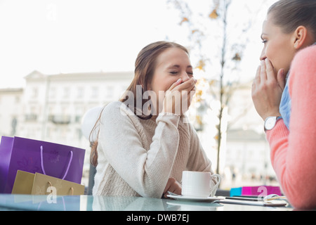 Professionnels des femmes partageant secrets at outdoor cafe Banque D'Images