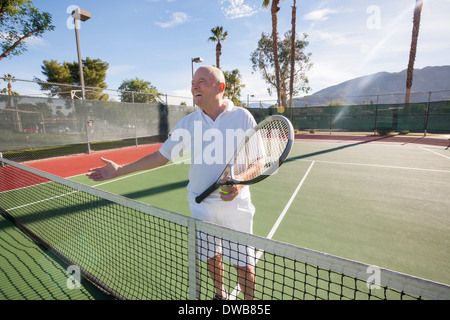 Happy senior male tennis player offrant handshake on court