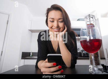 Beautiful young woman reading text message on smart phone au comptoir de la cuisine Banque D'Images