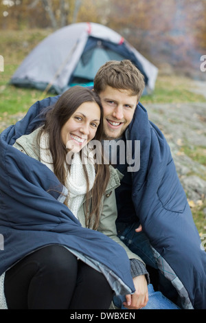 Portrait of happy couple wrapped in blanket contre tente à forest Banque D'Images