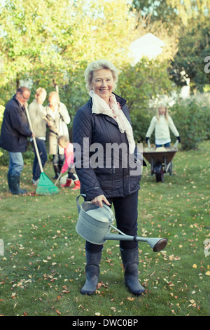 Portrait of senior woman watering can tout en faisant du jardinage avec la famille à la cour Banque D'Images