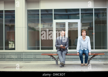 D'affaires et un jeune homme assis sur le banc de la gare Banque D'Images