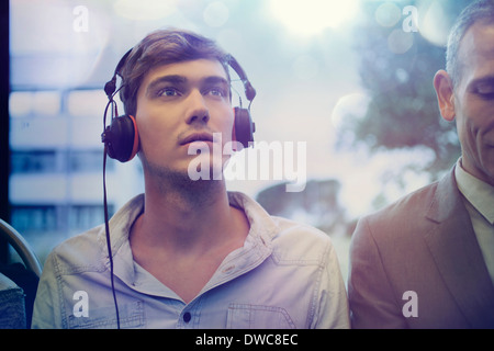 Jeune homme la rêverie et l'écoute au casque sur le train Banque D'Images