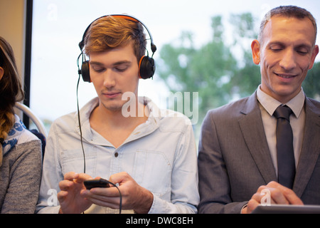 Jeune homme à l'écoute au casque et à l'aide du smartphone sur le train Banque D'Images