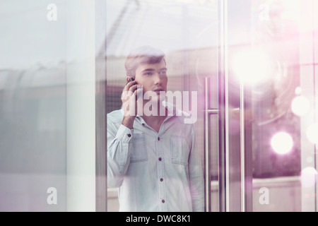 Jeune homme derrière verre réfléchissant lumineux parler sur smartphone Banque D'Images