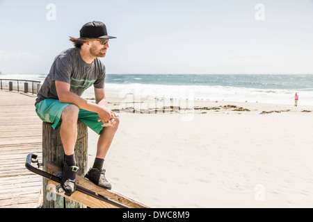 Young man sitting on wooden post, Laguna Beach, Californie, USA Banque D'Images