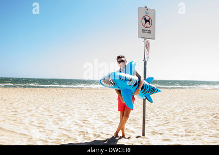 Young man holding inflatable requin tigre, Port Melbourne, Melbourne, Australie Banque D'Images