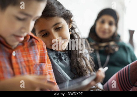 Frères et sœurs using digital tablet avec mère assis en arrière-plan Banque D'Images