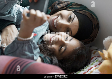 Mère et fille espiègle à l'aide de téléphone mobile dans la chambre Banque D'Images