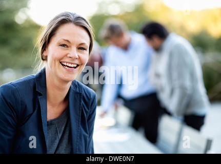 Portrait of businesswoman laughing at patio avec des collègues en arrière-plan Banque D'Images