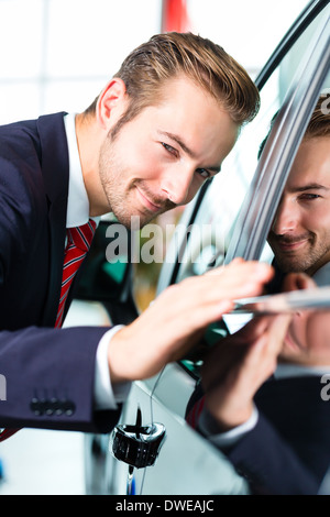 Vendeur ou vendeur de voiture dans l'agence de voiture présentant la peinture de voiture reflétant ses voitures neuves et d'occasion dans le showroom Banque D'Images