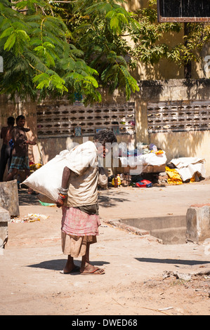 L'Inde Tamil Nadu Pondicherry Puducherry ploie la pauvre femme dame femme handicapé mobilité marcher transportant un grand sac sac blanc arbres scène de rue Banque D'Images