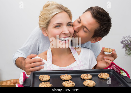 Man kissing woman's joue comme elle est titulaire d'biscuits fraîchement cuits au four dans la cuisine Banque D'Images