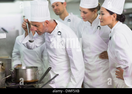 Dégustation chef cuisinier une soupe tandis que le personnel watch Banque D'Images