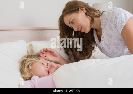 Mère regardant fille comme elle dort paisiblement dans son lit Banque D'Images