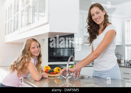 Girl aider sa mère pour laver les légumes dans la cuisine Banque D'Images