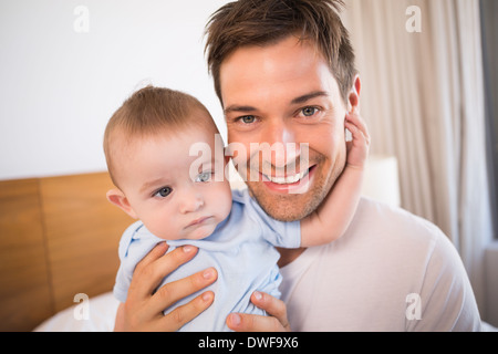Père assis sur le lit avec son bébé en bleu babygro Banque D'Images