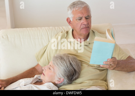 Senior man sitting on couch reading avec partner reposant sur lap Banque D'Images