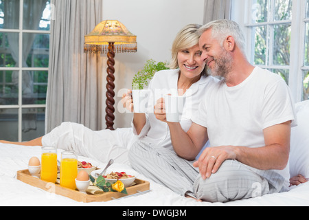 Smiling mature couple avec tasses à café sitting on bed Banque D'Images