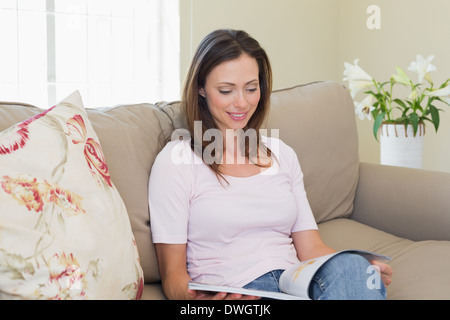 Smiling woman reading magazine dans la salle de séjour
