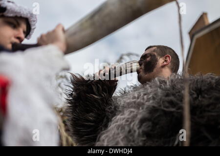 Mohacs (Hongrie). 4e Mar, 2014. Les cornes sont traditionnellement utilisées pour faire un appel avec sons mais l'homme dans le droit est en train de boire le vin de sa corne. Les festivités à Mohacs Fullmetal dans le sud de la Hongrie sont un carnaval de six jours à la fin de février pour marquer la fin de l'hiver, nommé pour les Busos, effrayant les gens costumés (traditionnellement, les hommes) de porter des masques en bois et de grands manteaux laineux. © Zsolt Repasy/ZUMA/ZUMAPRESS.com/Alamy fil Live News Banque D'Images