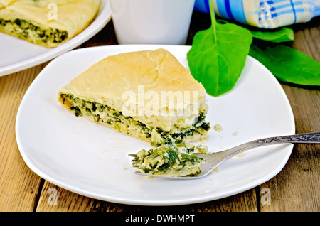 Tourte aux épinards et fromage sur une assiette, les feuilles d'épinards, tasse, tablier, serviette sur planche de bois Banque D'Images