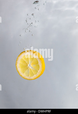 Tranches de citron de tomber dans l'eau sur un fond blanc. Banque D'Images