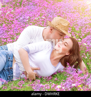 Jeune famille s'embrasser dans le jardin, couché sur le champ de fleurs de printemps à chaude journée ensoleillée, doux sentiments, vie heureuse Banque D'Images