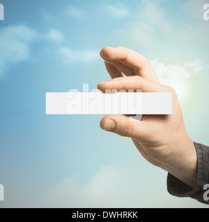 Une main tenant une carte vierge avec un ciel bleu à l'arrière-plan avec des nuages et du soleil. Banque D'Images