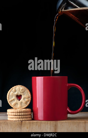 Verser du café d'une cafetière dans une tasse rouge et biscuits Banque D'Images