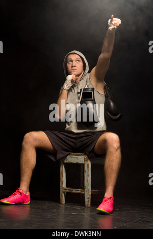 Boxer sitting attendre sur un banc de bois dans un coin sombre pointant vers le ciel pendant qu'il s'psychés avant un combat qui demande de l'aide à gagner le match. Banque D'Images